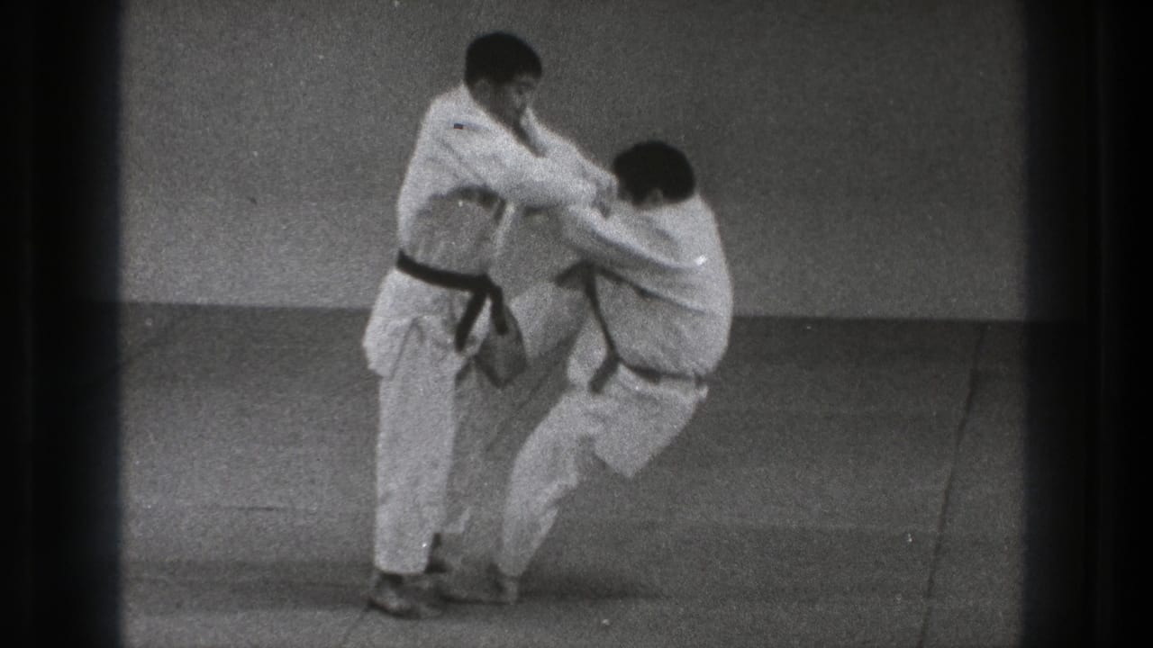 During the judo-style technique, one man lowers toward the mat while the standing practitioner controls the grip and balance.