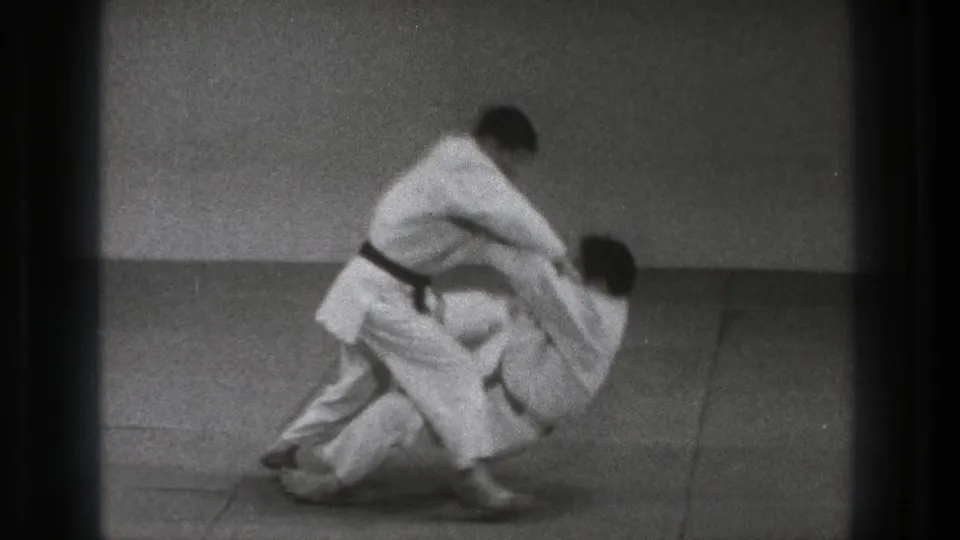The throw resolves with one man on the mat and the black-belt practitioner standing above him in the short 1971 Tokyo training sequence.