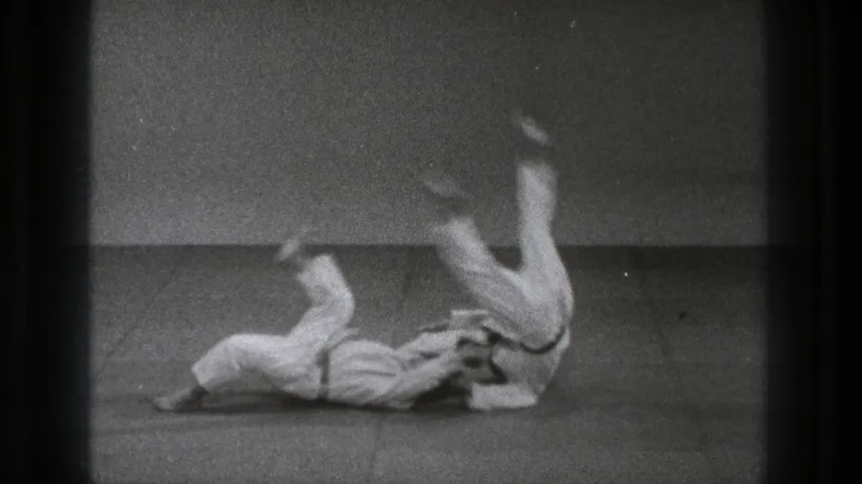 At the end of the 1971 Tokyo throw sequence, one practitioner lands with legs raised while his partner lies on the mat nearby.