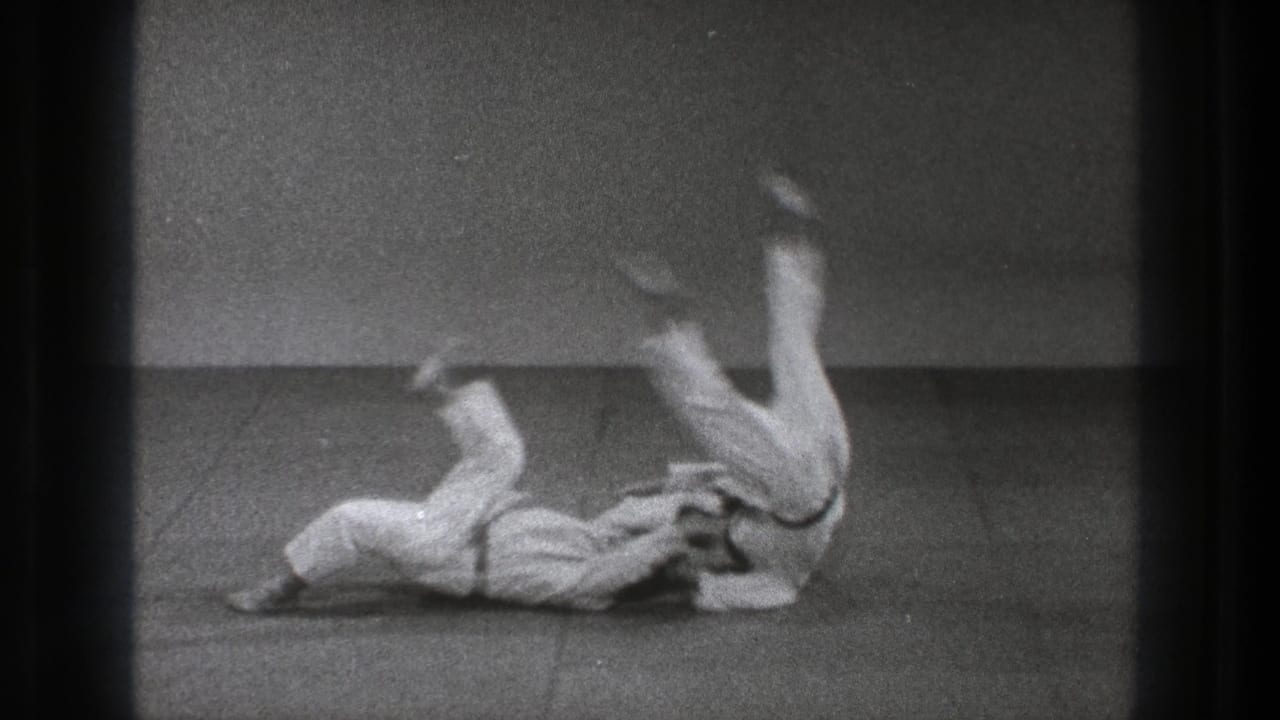 Two judo practitioners in white gi complete a throw on a mat.