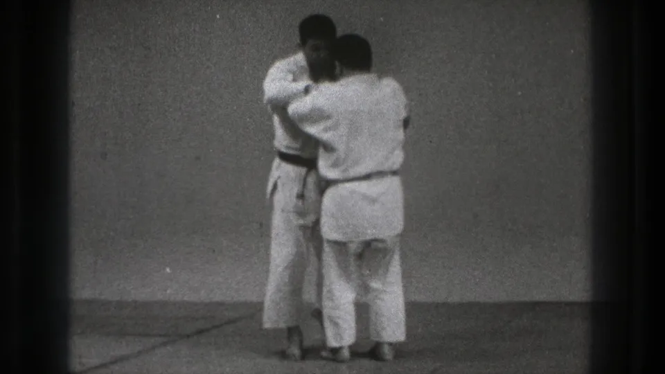 Tokyo 1971 8mm frame of two adult judo practitioners in white gi holding a close grappling position.