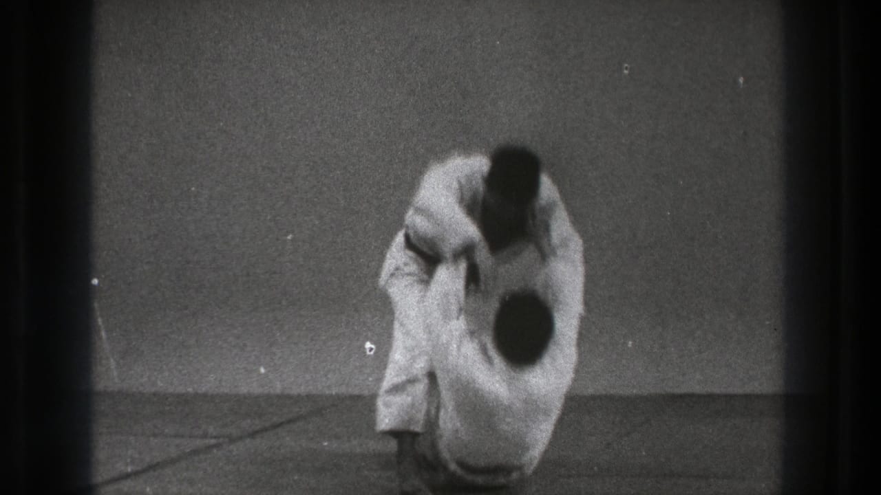 The throw concludes as one practitioner is brought down toward the mat while the other remains above him in the 1971 Tokyo clip.