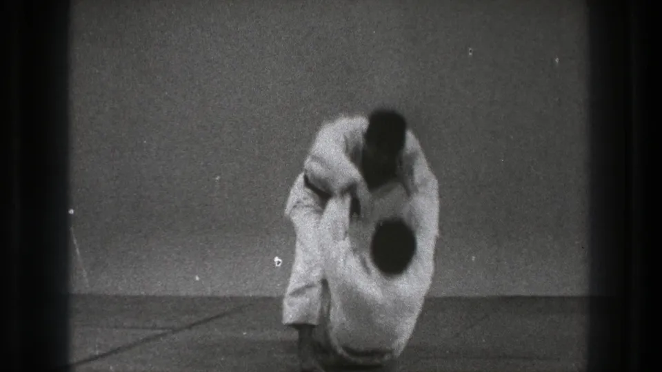 The throw concludes as one practitioner is brought down toward the mat while the other remains above him in the 1971 Tokyo clip.