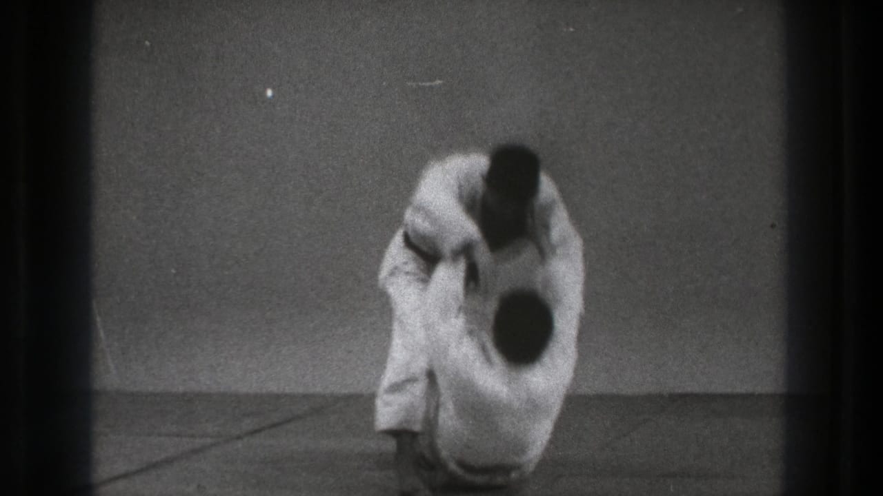 Two men in white judo uniforms grapple on a mat as one begins a throw.