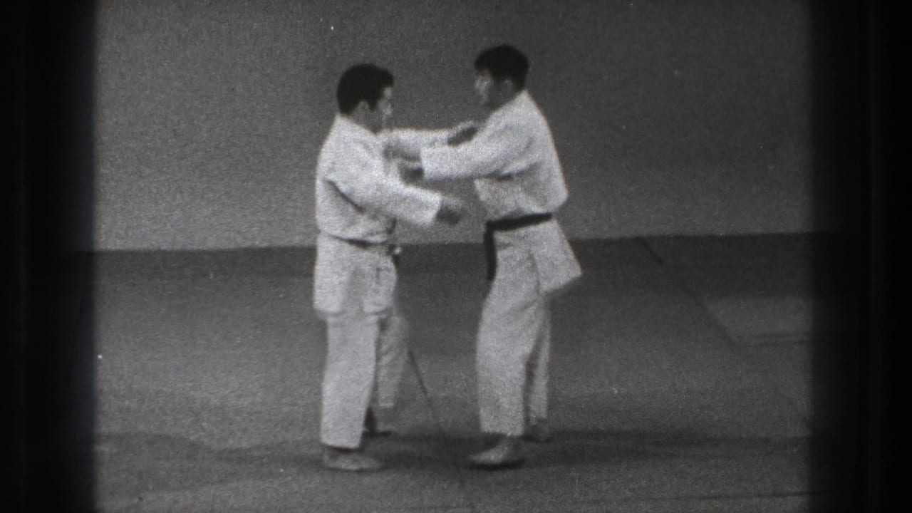 Two men in white martial arts gi face each other on a dojo mat.
