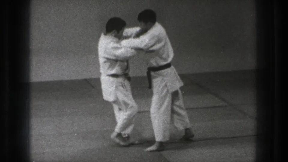 The final frame shows the two adult men in white gi maintaining grips as they practice on the dojo mat in archival 1971 Tokyo footage.