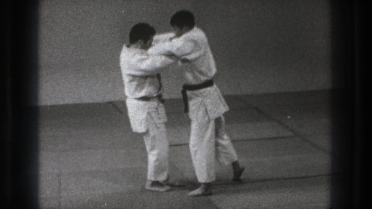 Two men in white judo uniforms grip each other on indoor mats.
