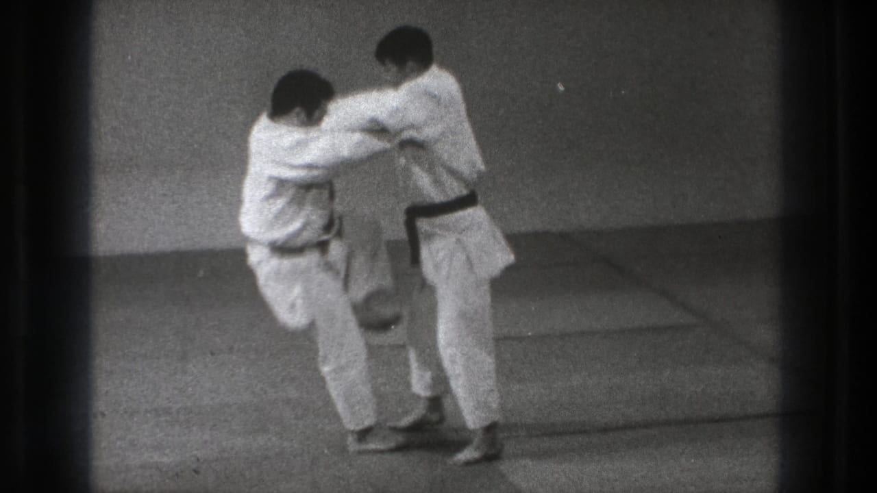 The 1971 Tokyo judo practice shows one participant lifting his knee as the pair maintain close grips on the mat.