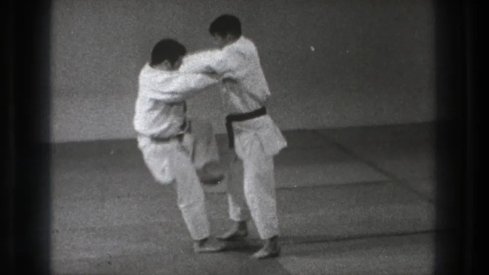 The 1971 Tokyo judo practice shows one participant lifting his knee as the pair maintain close grips on the mat.