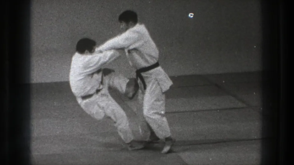 During the Tokyo judo demonstration, one man bends lower while his partner turns into the throw on the indoor mats.