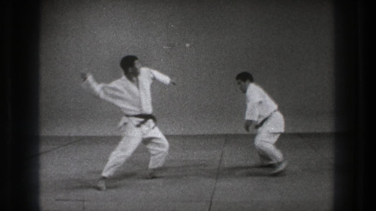 1971 Tokyo 8mm frame showing a judoka stepping in with arms raised as the second practitioner lowers into a defensive stance.