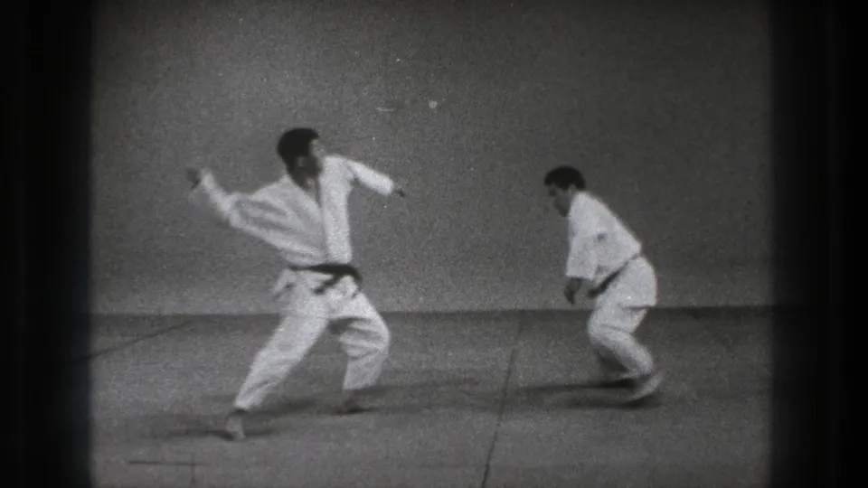 1971 Tokyo 8mm frame showing a judoka stepping in with arms raised as the second practitioner lowers into a defensive stance.