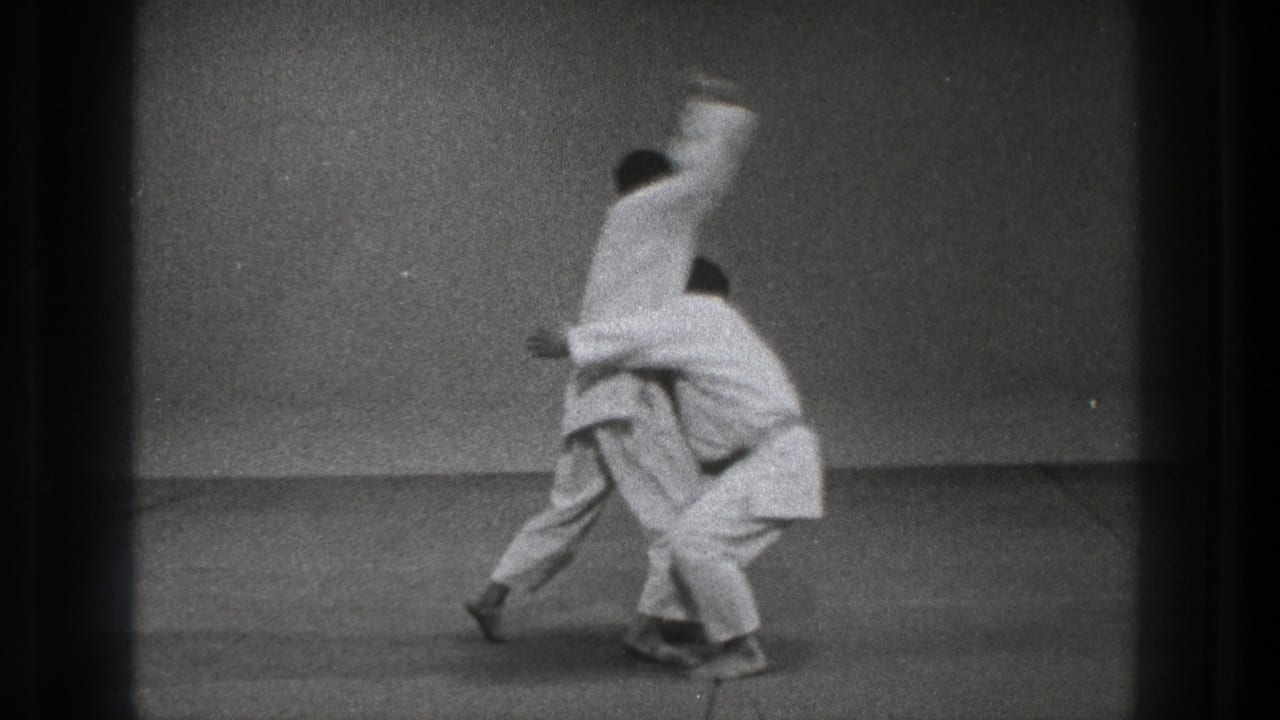 1971 Tokyo 8mm frame showing the Ura Nage throw in progress, with one practitioner lifting the other against a plain dojo wall.