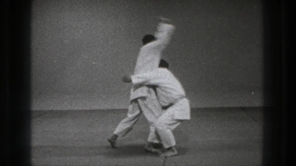 1971 Tokyo 8mm frame showing the Ura Nage throw in progress, with one practitioner lifting the other against a plain dojo wall.