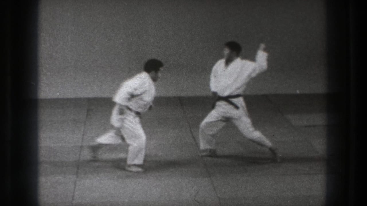 Two adult men in white gi stand facing each other on a practice mat in the 1971 Tokyo clip.