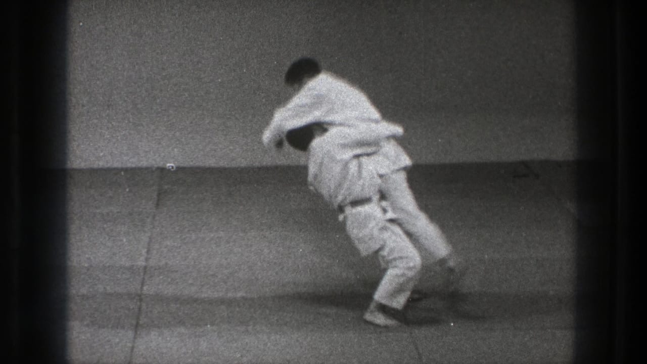 Two men in white martial arts uniforms begin a throw on a grey mat.