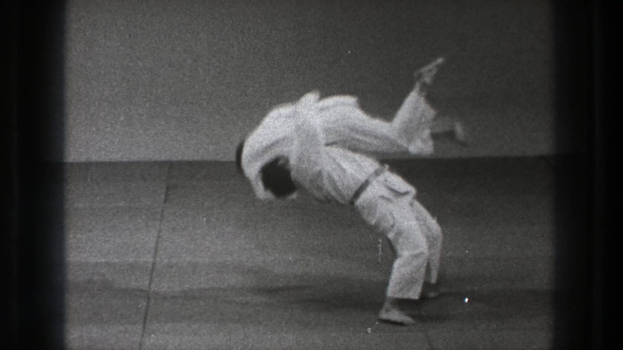 A white-uniformed practitioner lifts an opponent over his back during a slow-motion martial arts throw in the Tokyo 1971 clip.