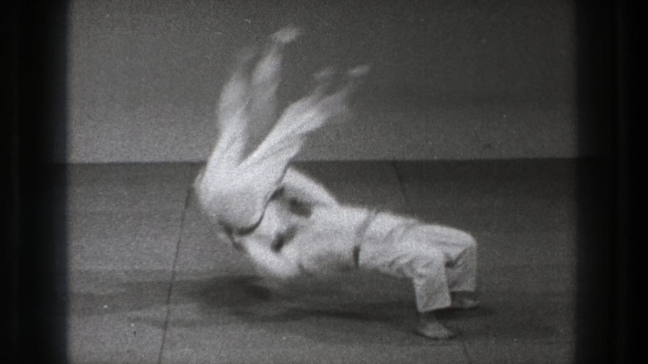 The slow-motion sequence shows the thrown adult practitioner rotating above the mat while the thrower remains braced below.