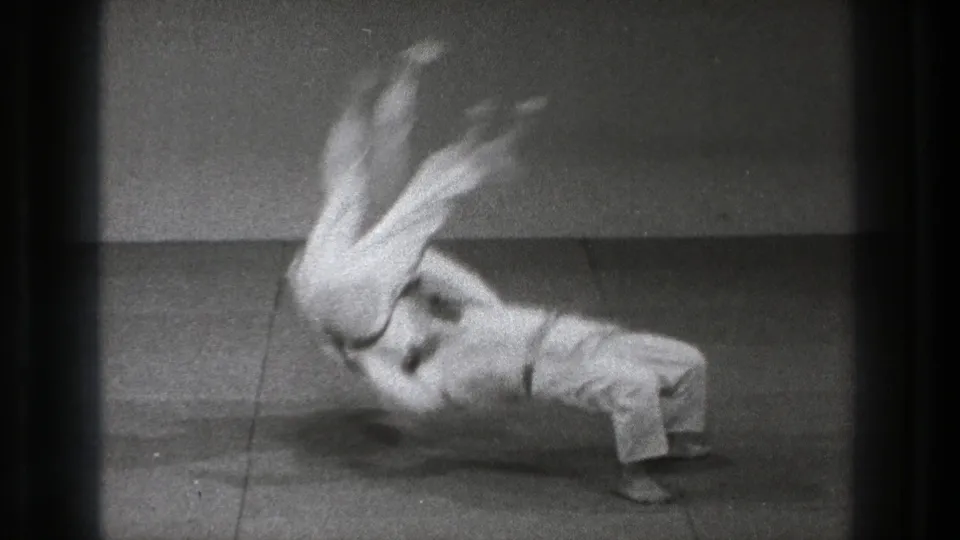 The slow-motion sequence shows the thrown adult practitioner rotating above the mat while the thrower remains braced below.
