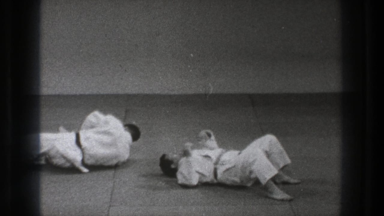 Two men in white martial arts uniforms lie on a mat during practice.
