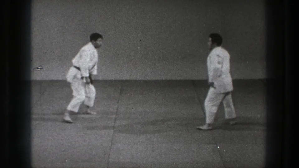 In the final frame, two adult men in white gi and dark belts face each other on the dojo mat in the 1971 Tokyo footage.