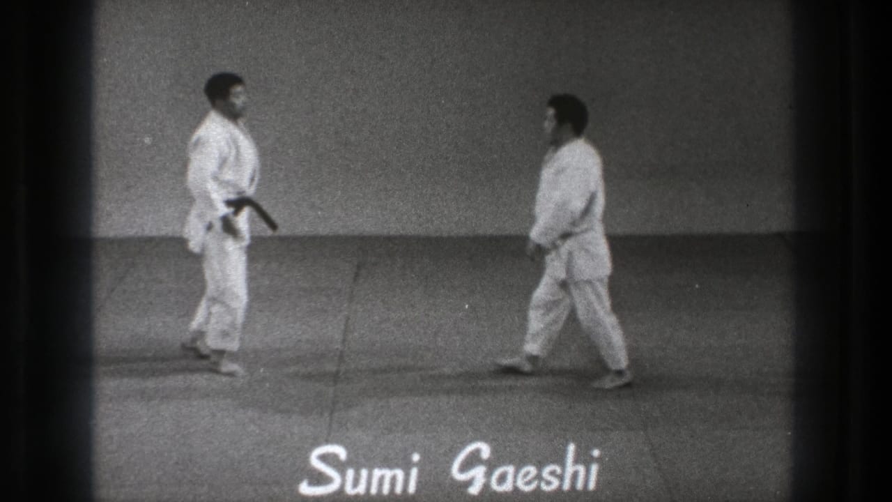 Two men in white gi face each other on an indoor mat with Sumi Gaeshi text below.