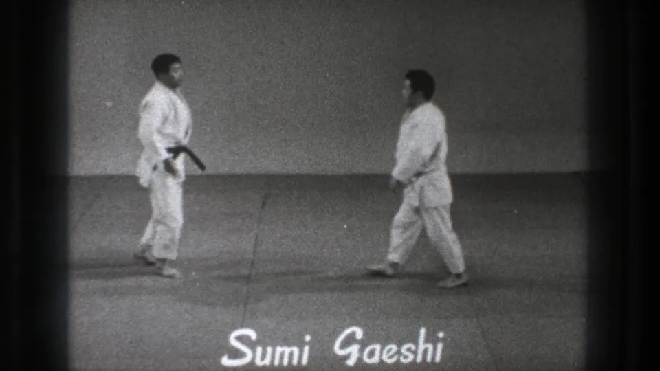 Two adult martial arts practitioners in white gi face each other in a Tokyo indoor dojo scene from the 1971 8mm clip.