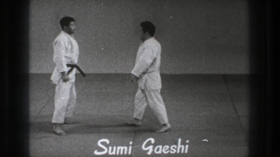 Two adult practitioners pause opposite each other on the mat as the Sumi Gaeshi label appears in the 1971 Tokyo martial arts clip.