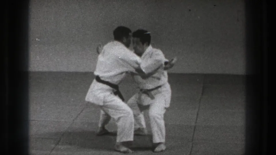 The practitioners grip each other and drop into the throwing motion during the Sumi Gaeshi demonstration in the 1971 Tokyo clip.
