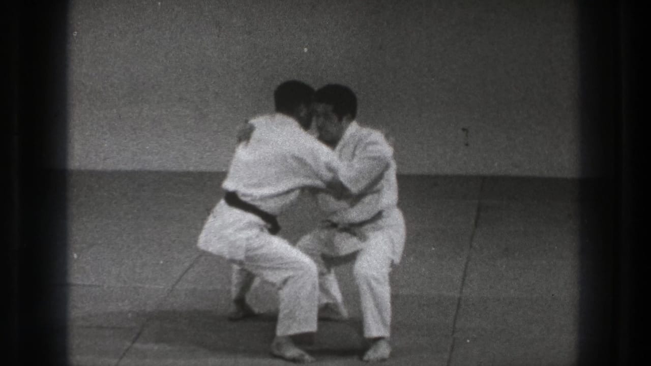 Two karate practitioners face each other closely in a low grappling stance on a mat.