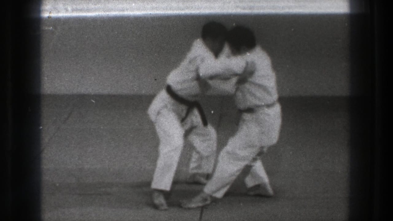 Two adult men in white gi shift their footing during a karate defense demonstration in the 1971 Tokyo indoor footage.