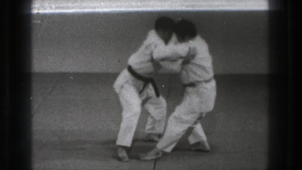 Two adult men in white gi shift their footing during a karate defense demonstration in the 1971 Tokyo indoor footage.