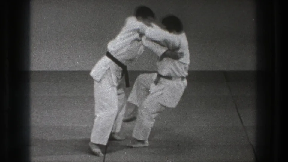 In Tokyo 1971 8mm footage, two martial artists in white uniforms begin a hip throw on a grey mat.