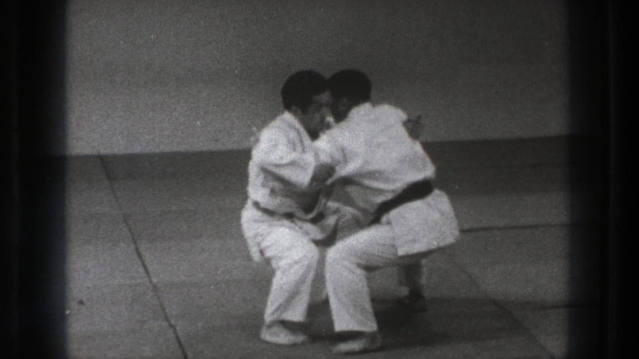 The martial arts drill continues as the two men crouch low on the mat, maintaining close arm contact in the 1971 Tokyo footage.