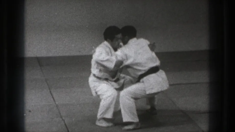The martial arts drill continues as the two men crouch low on the mat, maintaining close arm contact in the 1971 Tokyo footage.