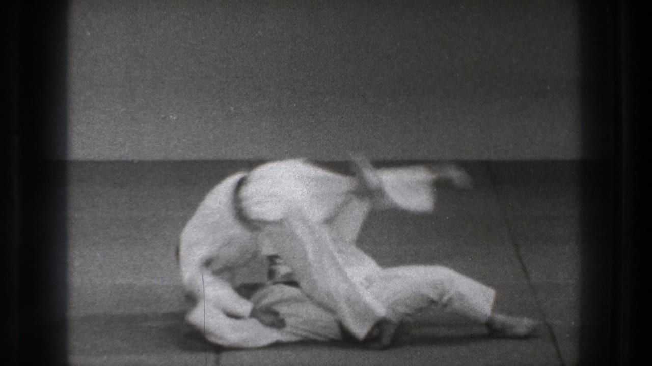 Two judo practitioners in white uniforms grapple low on a mat.