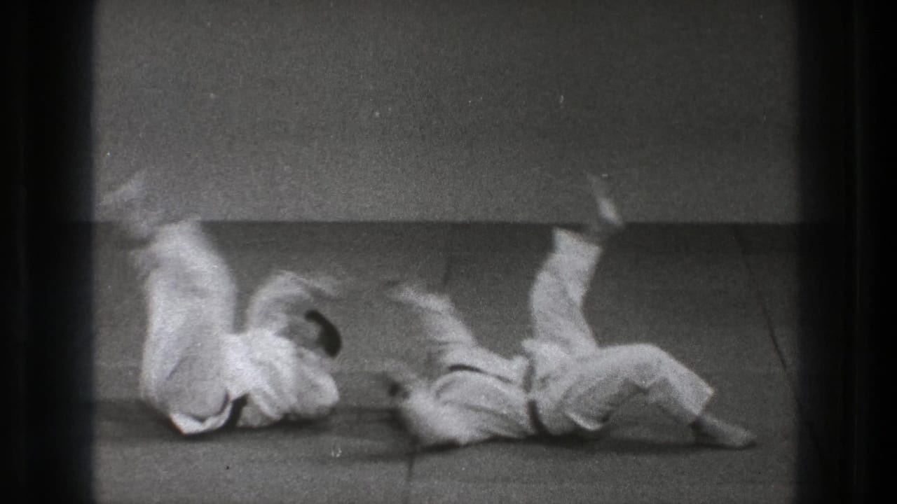 Two men in judogi roll on the dojo mat during judo practice in 1971 Tokyo home-movie footage.