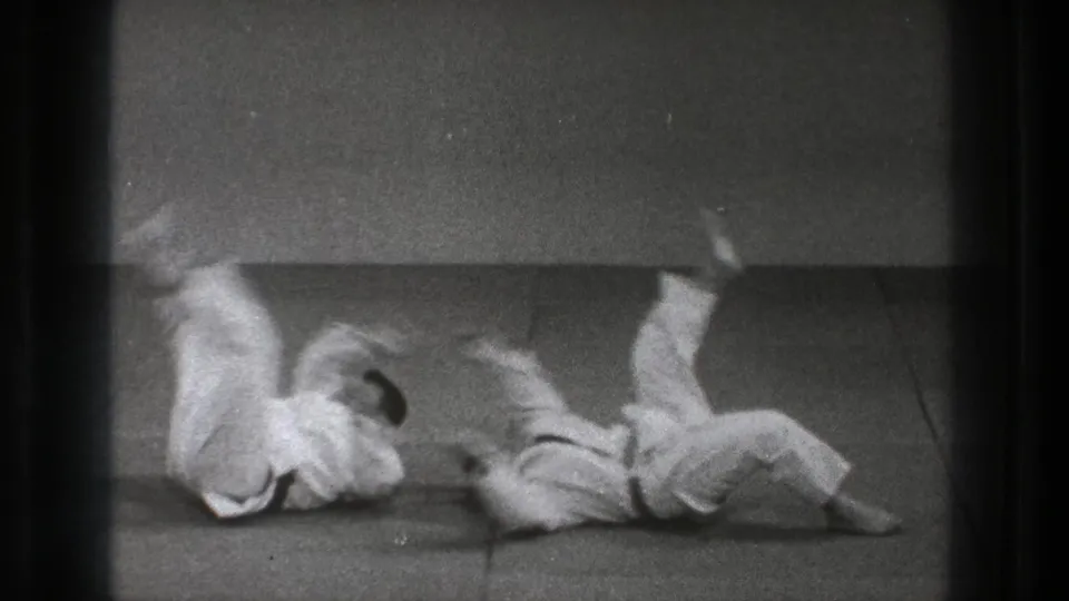 Two men in judogi roll on the dojo mat during judo practice in 1971 Tokyo home-movie footage.