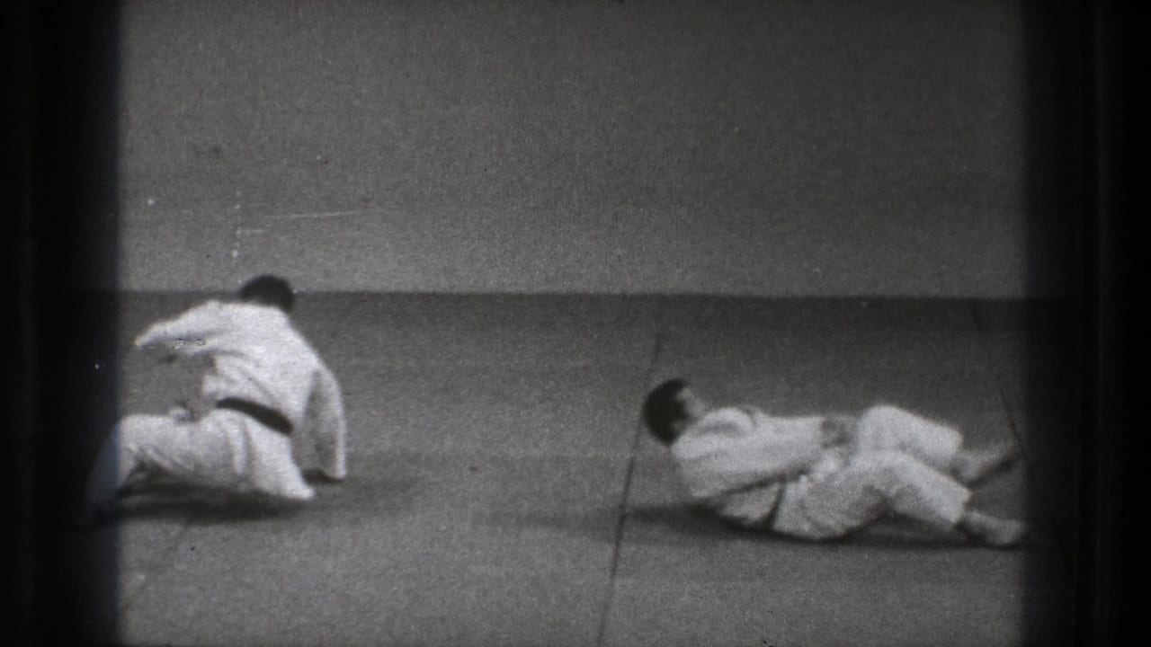 After a grappling exchange, one judo practitioner sits up while the other lies on the mat in the Tokyo dojo footage.