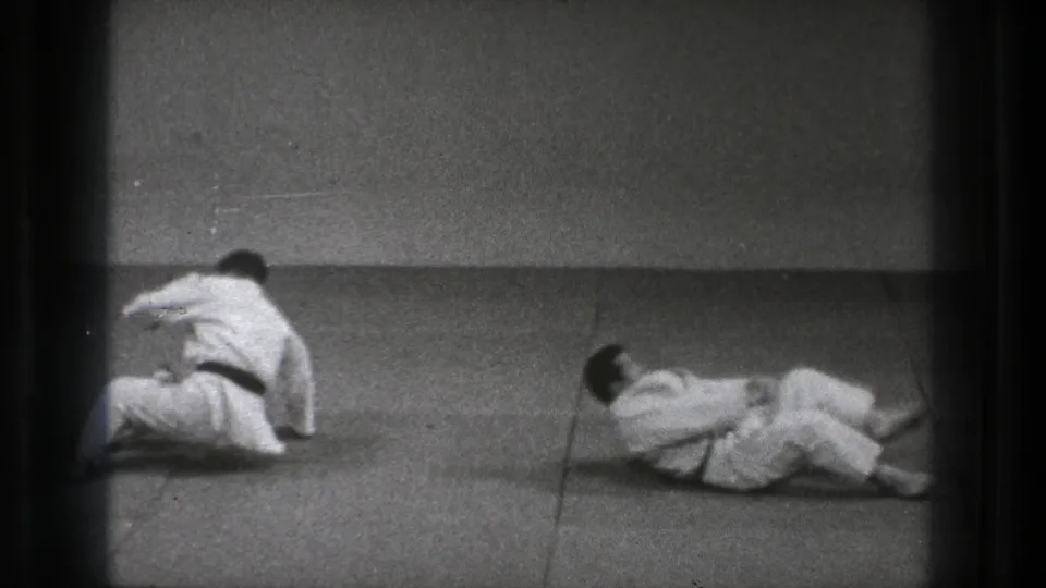 After a grappling exchange, one judo practitioner sits up while the other lies on the mat in the Tokyo dojo footage.