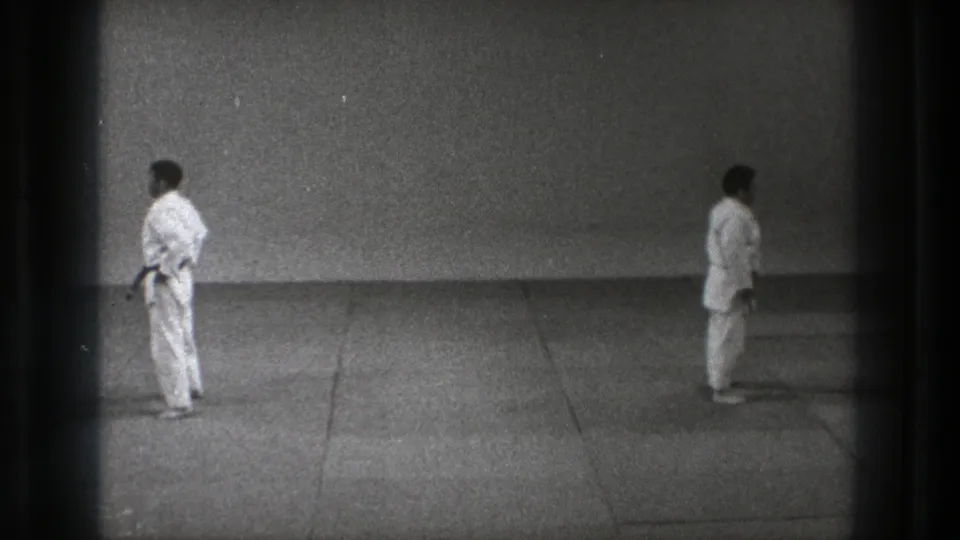 Two martial arts practitioners in white gi stand facing away from each other on a simple mat in Tokyo, Japan, 1971 footage.