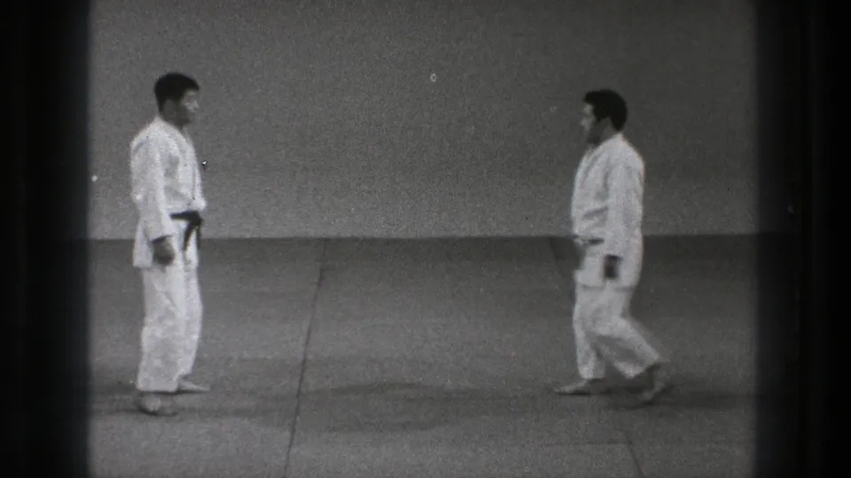 Two adult men in white gi move into closer range on the matted floor during a martial-arts demonstration in the 1971 Tokyo clip.