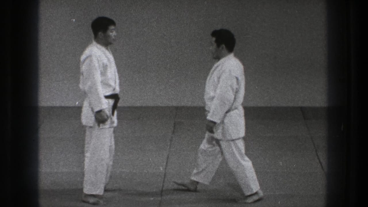 Close view of two adult practitioners in white gi on a mat, with one stepping forward as the paired technique setup begins.
