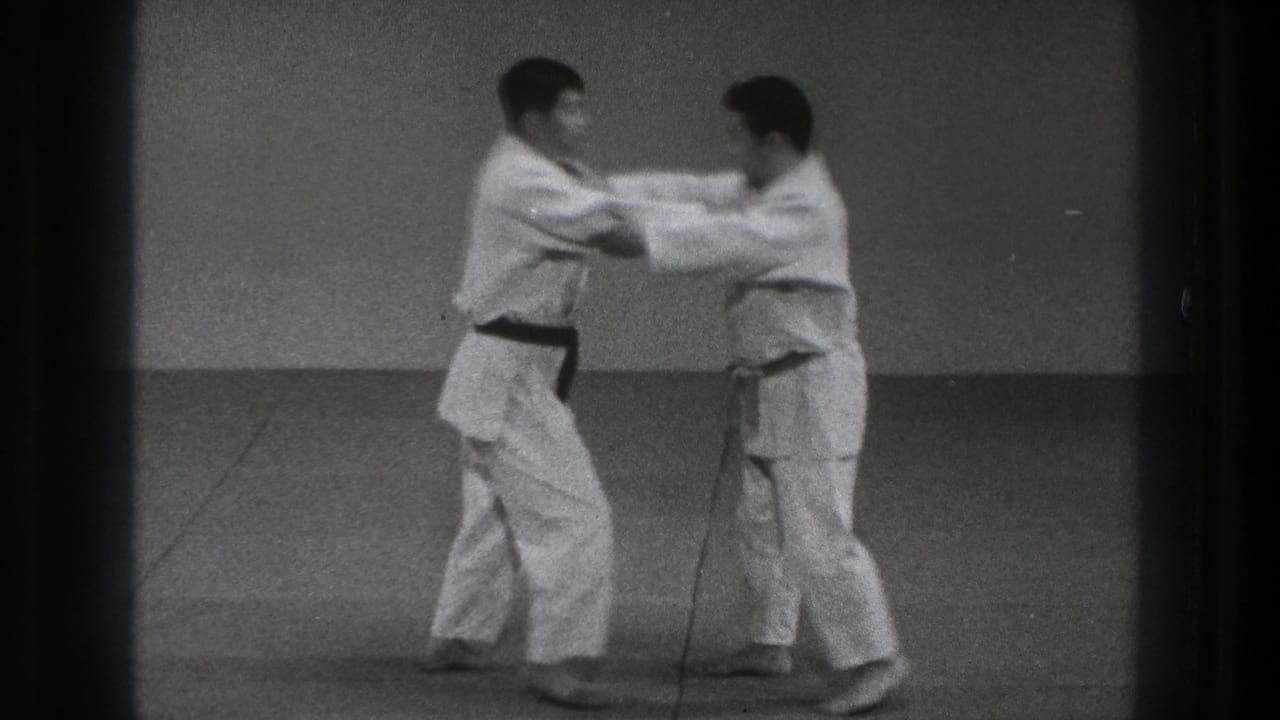 Two karate practitioners in white gi make sleeve or arm contact while stepping into a controlled drill.