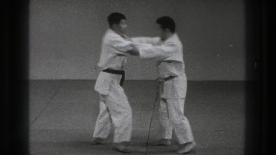 Two karate practitioners in white gi make sleeve or arm contact while stepping into a controlled drill.