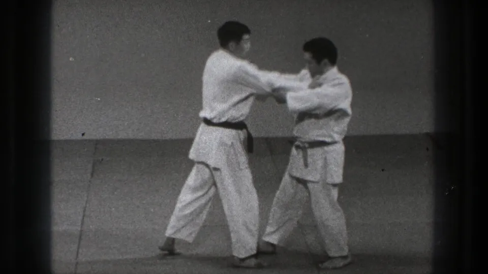 The partner drill continues as two men in gi hold arm contact and shift weight across the mat in the Tokyo 1971 clip.