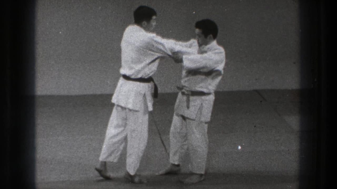 In a Tokyo dojo setting, two adult practitioners in white gi face each other on tatami mats at the start of a throw sequence.