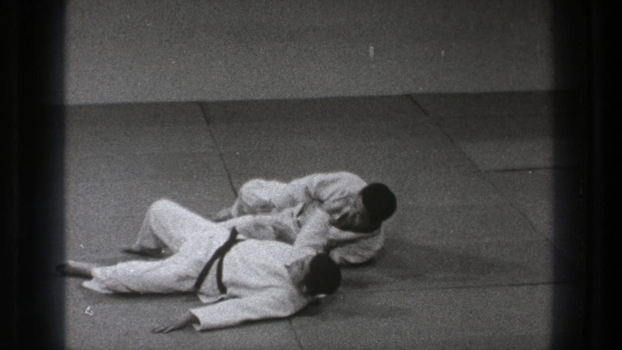 Both practitioners remain low on the tatami in a follow-through position after the throw, with one controlling the other's upper body.