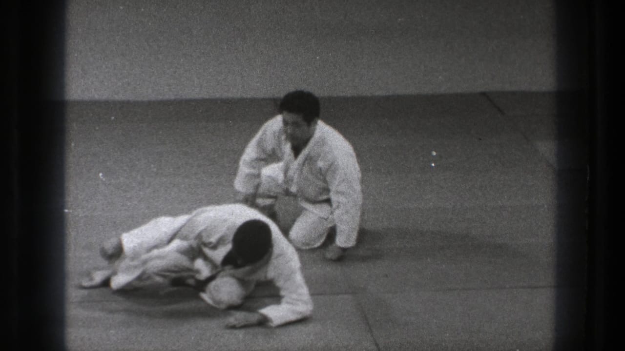 At the end of the Tokyo training sequence, one gi-clad practitioner sits back while the other pushes up from the mat.