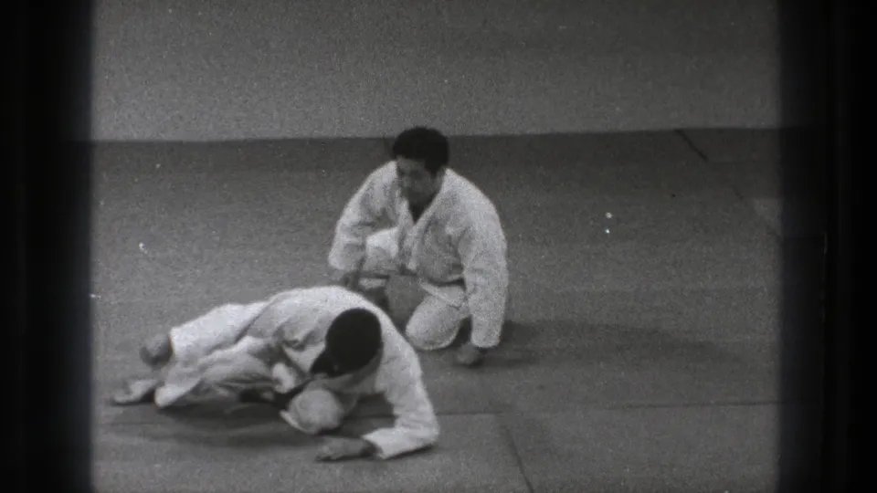 At the end of the Tokyo training sequence, one gi-clad practitioner sits back while the other pushes up from the mat.